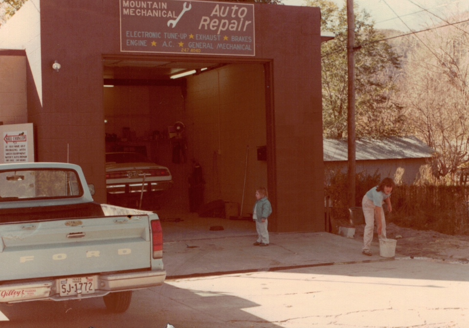 Small auto repair garage with a pickup truck parked outside and two people near the entrance