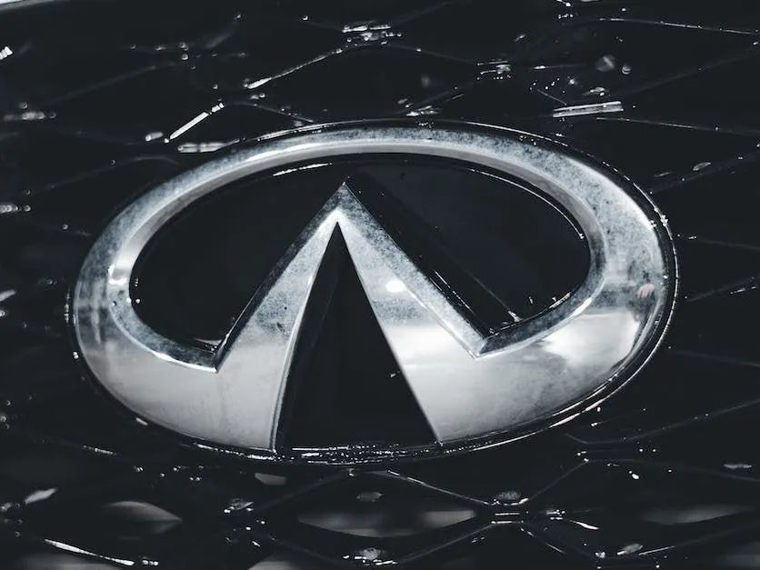 Silver Infiniti logo on a black car hood with visible scratches and reflections