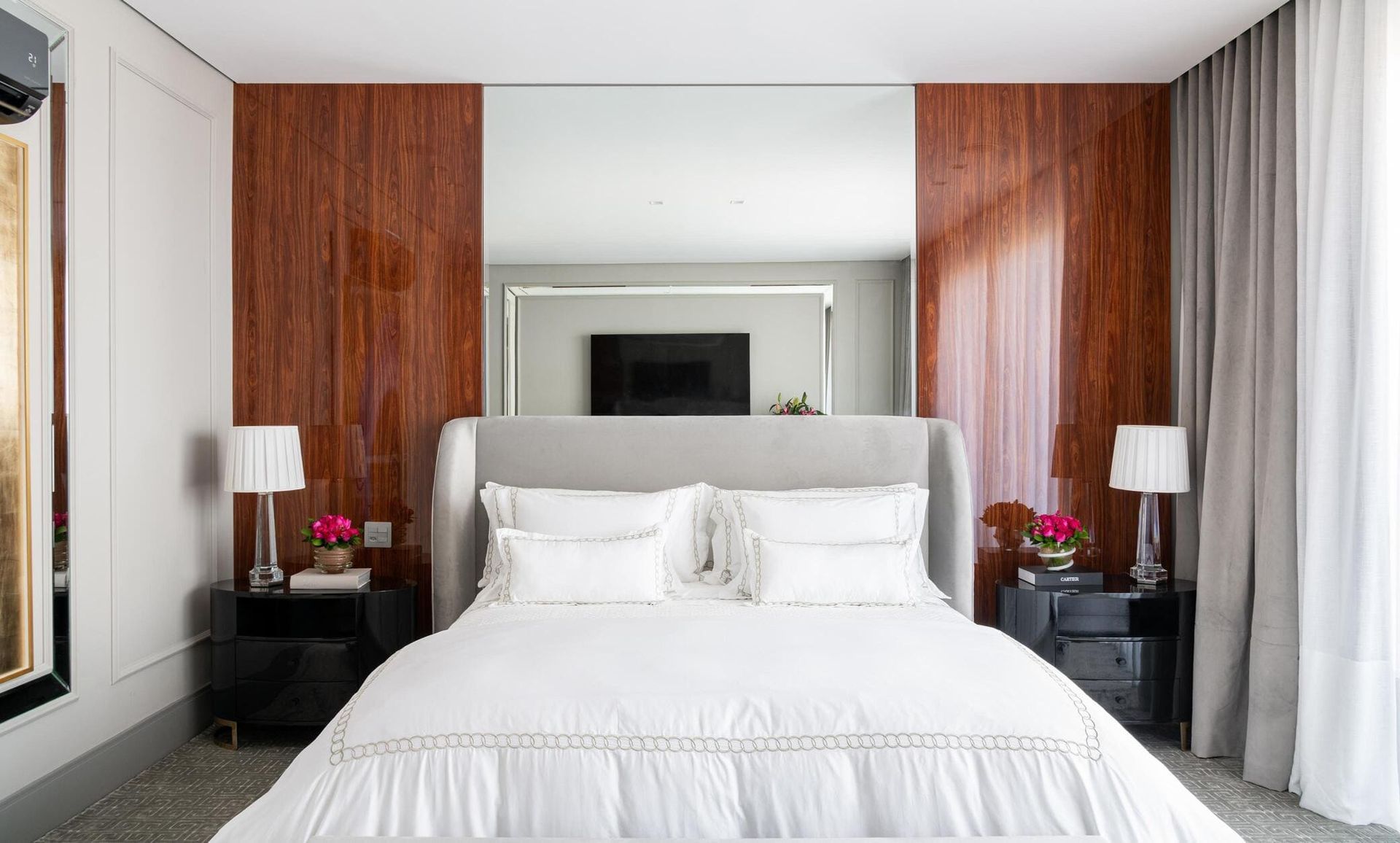 Um quarto com uma cama, mesas de cabeceira, abajures e um grande espelho na parede.