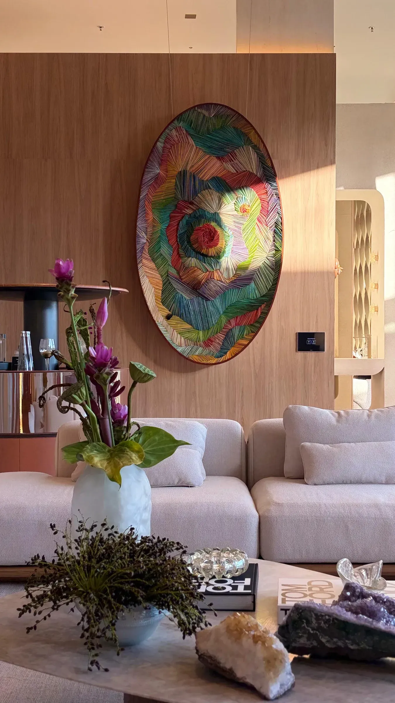 Sala de estar moderna com sofá bege, arranjo floral, mesa de centro e arte de parede circular colorida.