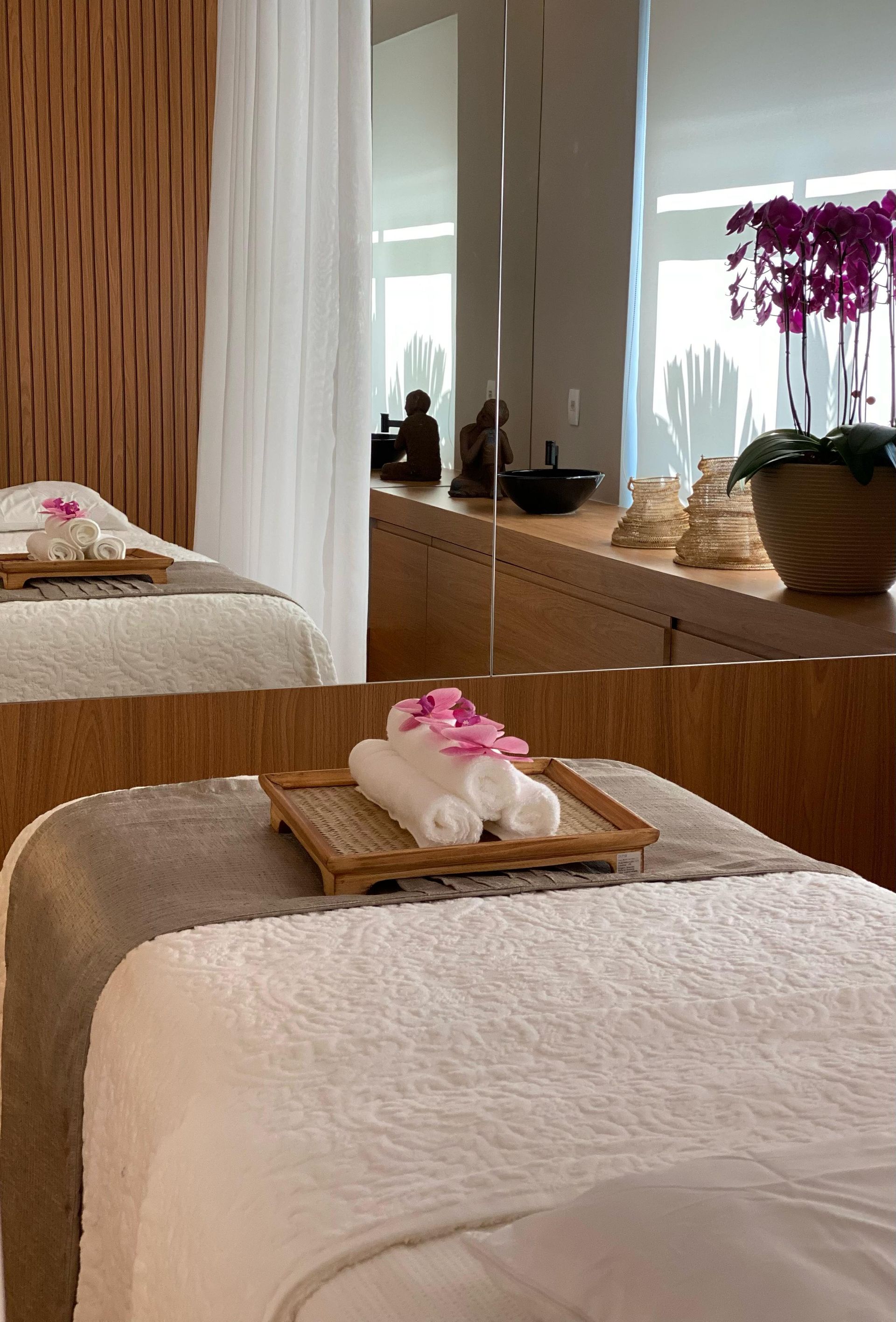 Uma mesa de massagem com toalhas e flores em frente a um espelho.
