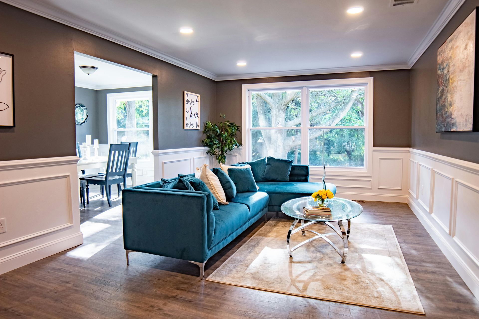 Bright living room with teal sofa, large windows, white wainscoting, and coffee table on a cream rug