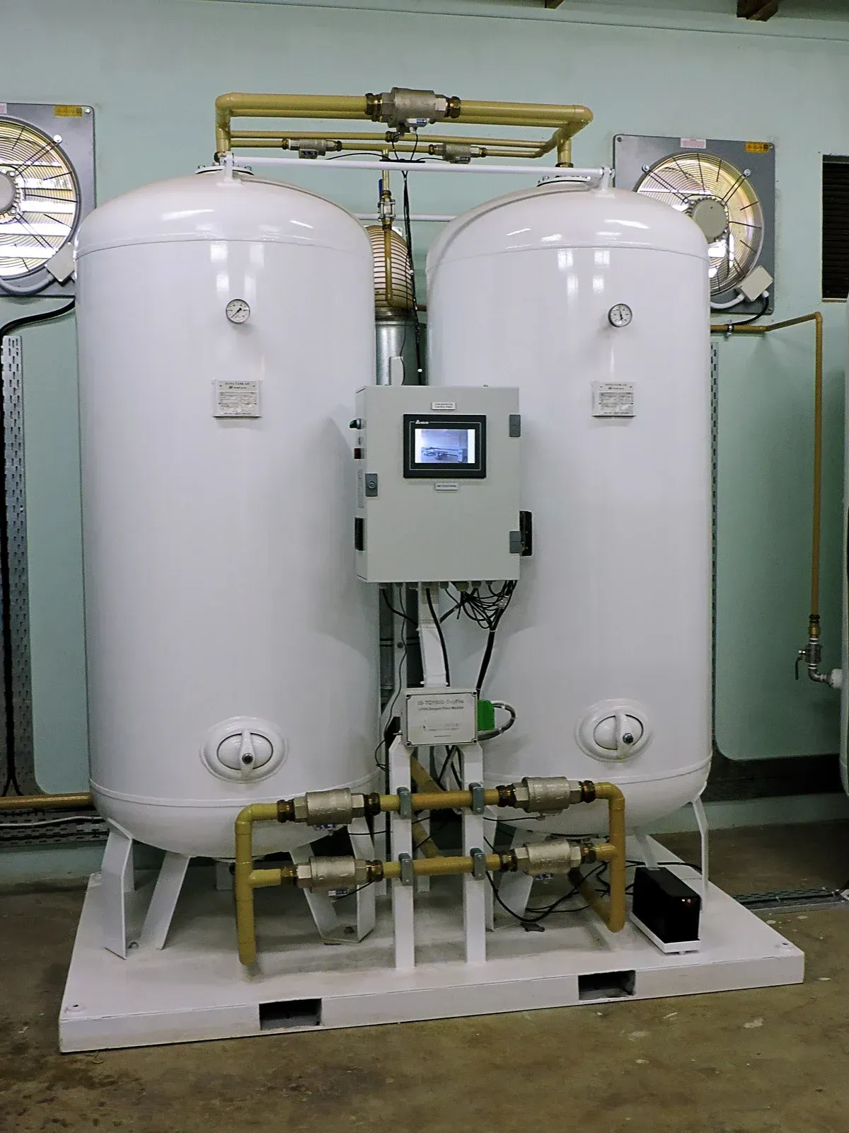 Two large white industrial tanks with a central control panel and piping in a factory setting
