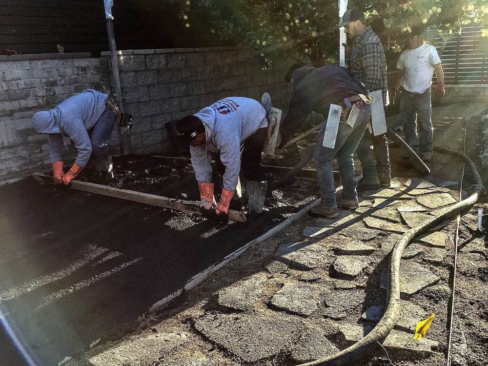 A group of men are working on a concrete driveway.