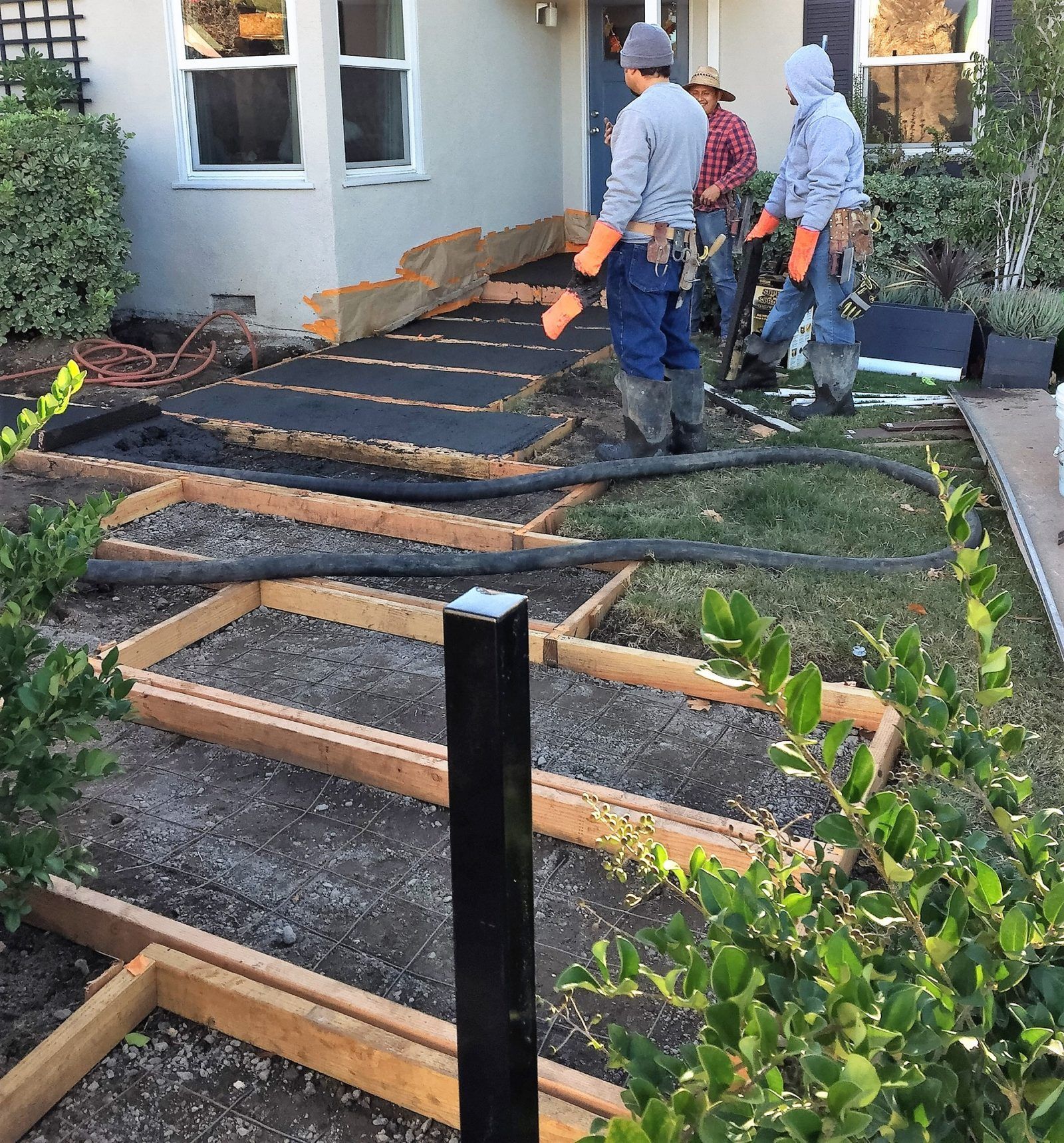 A group of men are working on a concrete walkway in front of a house.