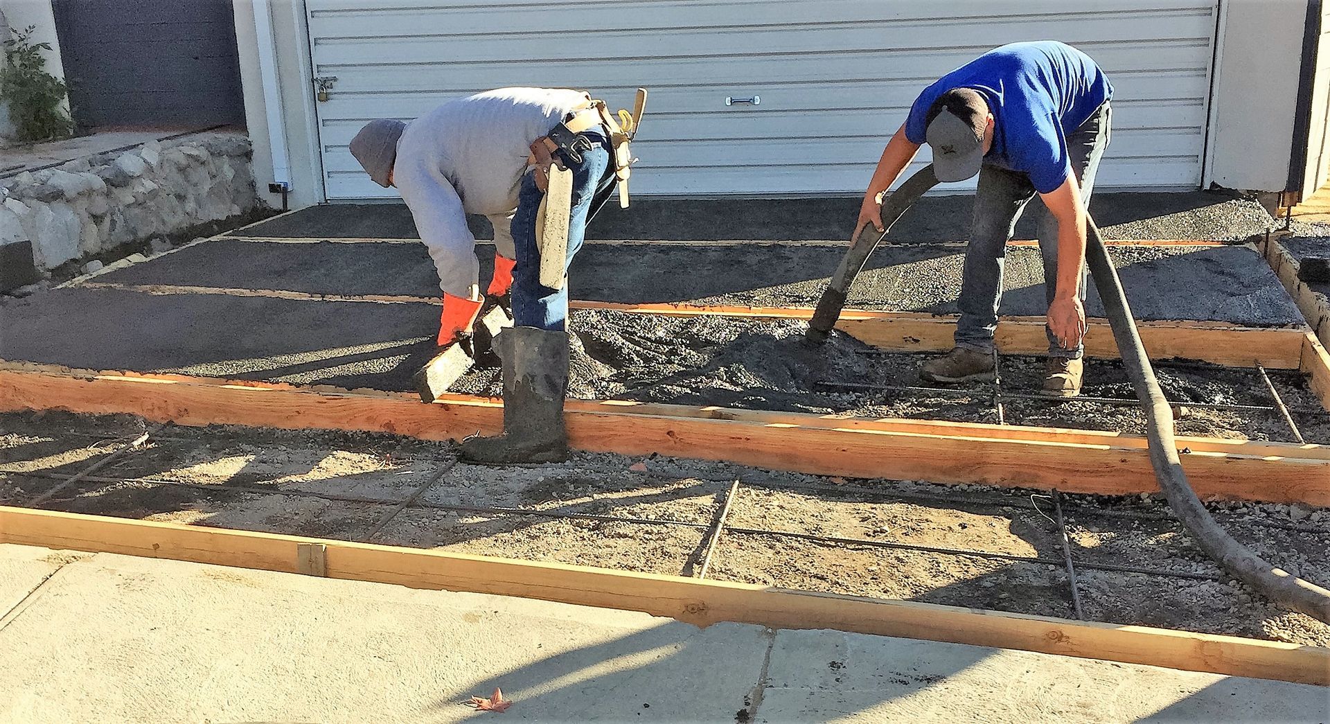 Two men are working on a concrete driveway in front of a garage.