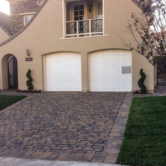 A house with a brick driveway and two white garage doors