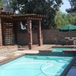 A large swimming pool with a pergola and umbrellas in a backyard.