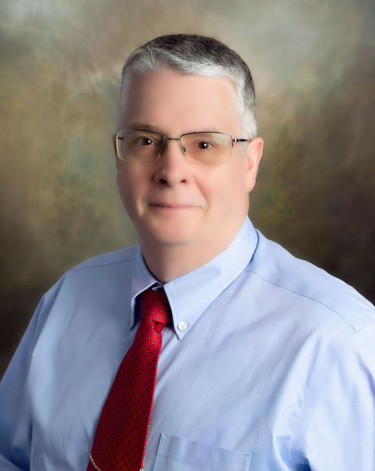 A professional headshot of a person wearing glasses, a light blue dress shirt, and a red tie against a mottled background.