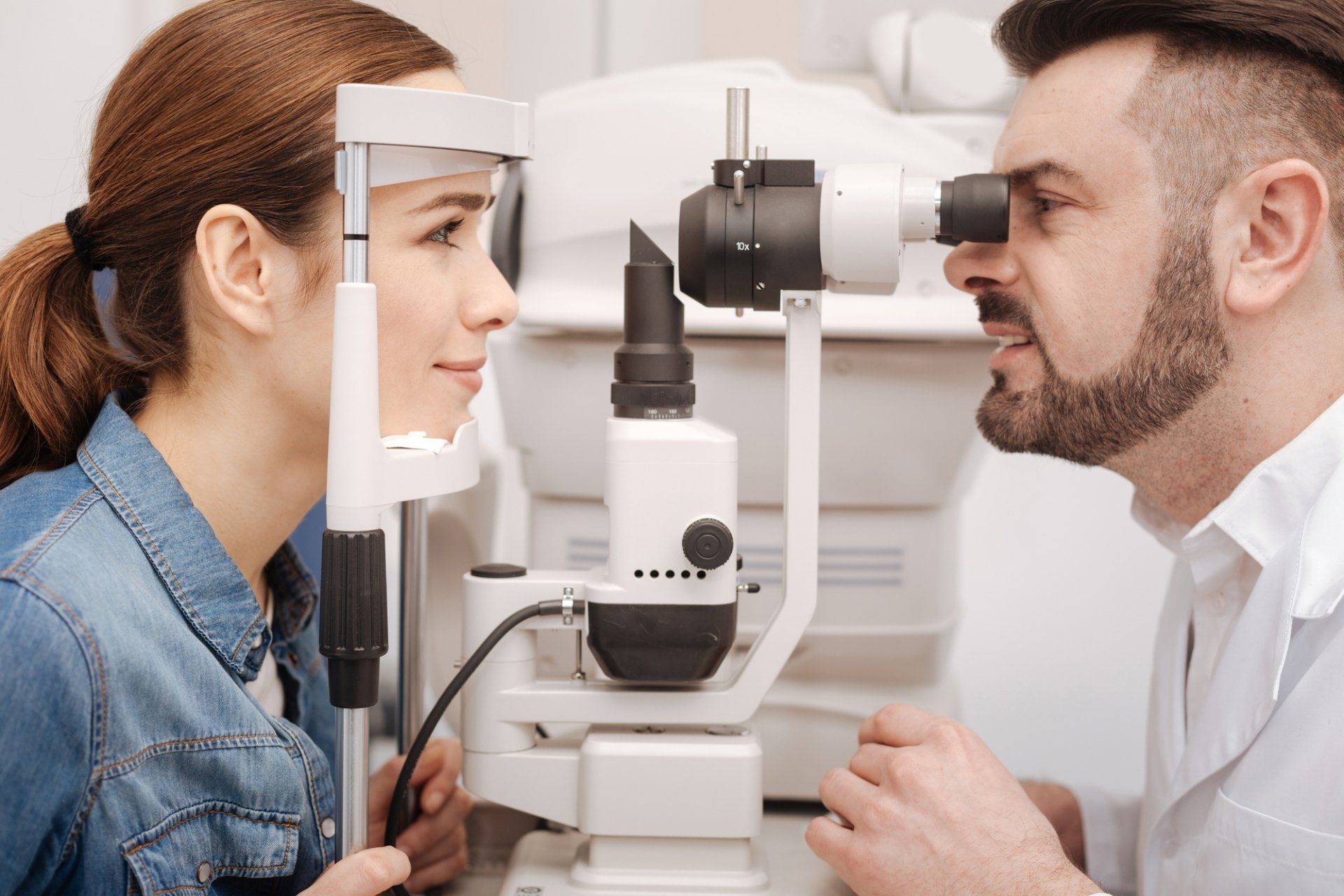 An optometrist uses a slit lamp microscope to examine a patient's eye in a clinical office setting.