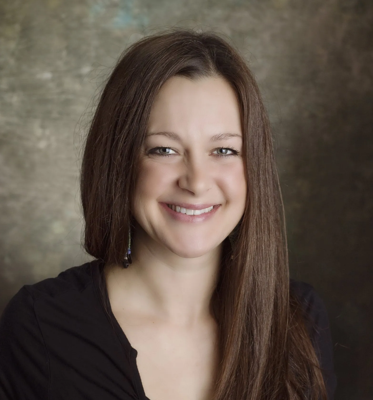 A person with long brown hair smiling against a textured, mottled brown backdrop.