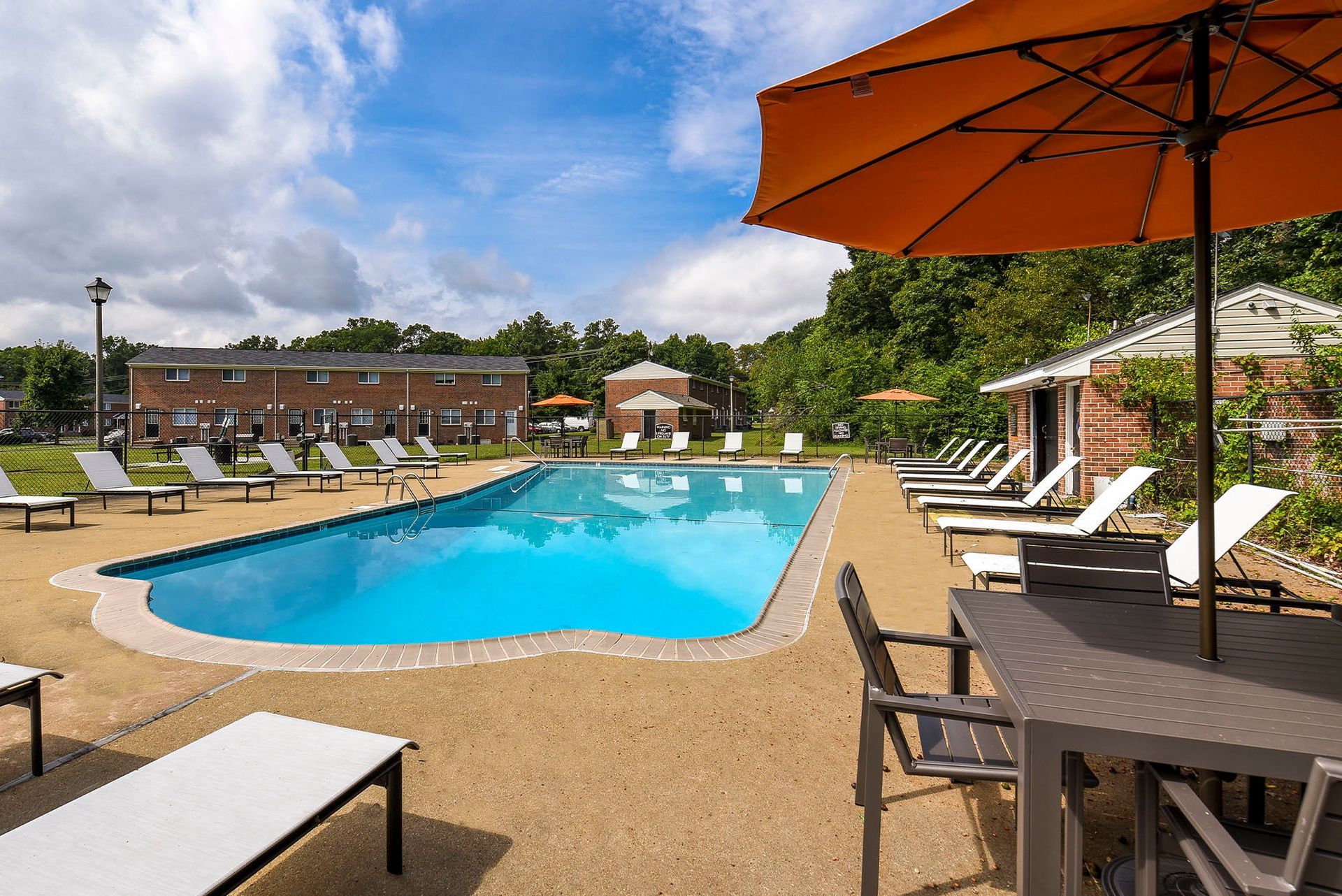 Pool with lounge chairs and orange umbrellas; brick buildings in background.
