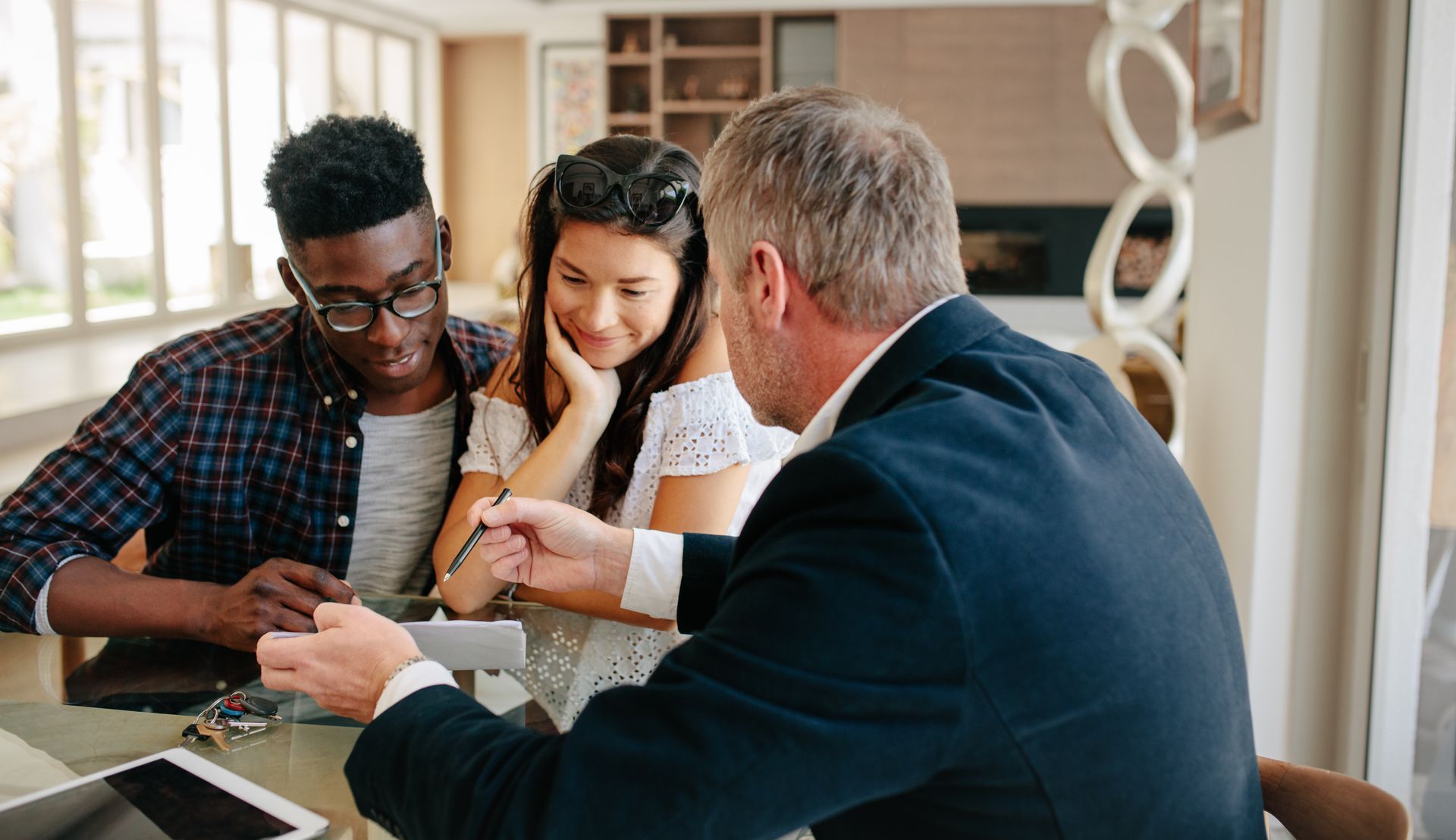 Three people in a meeting reviewing documents at a table in a bright office