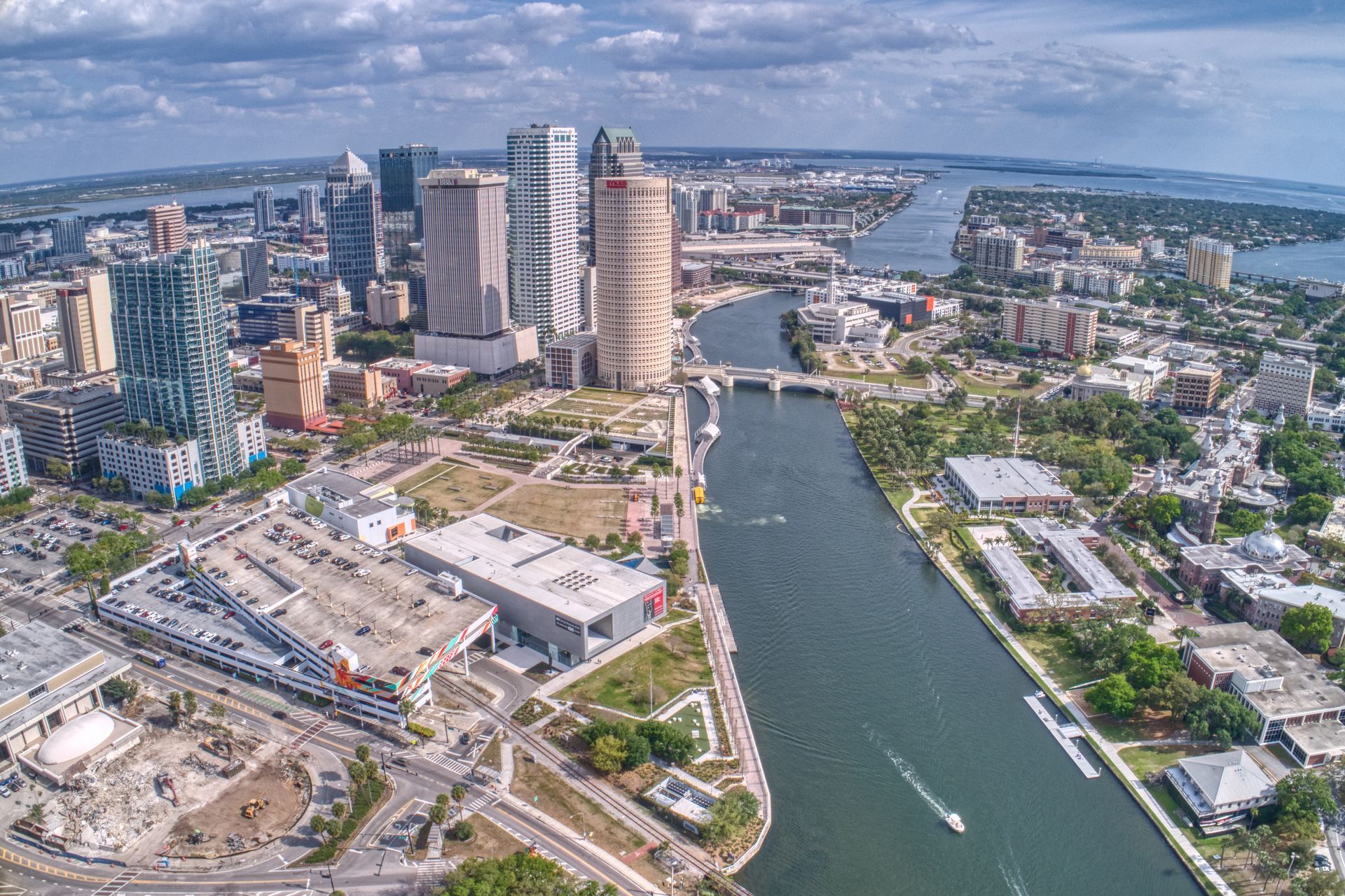 Aerial view of a riverfront city skyline with high-rise towers, bridges, and boats on the water.