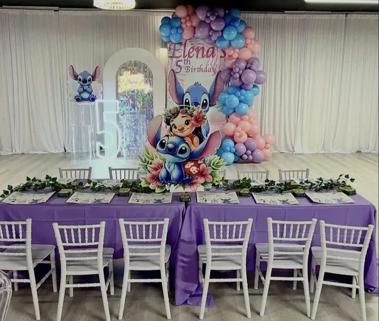 Stitch-themed birthday party setup with purple table, white chairs, and balloon arch backdrop