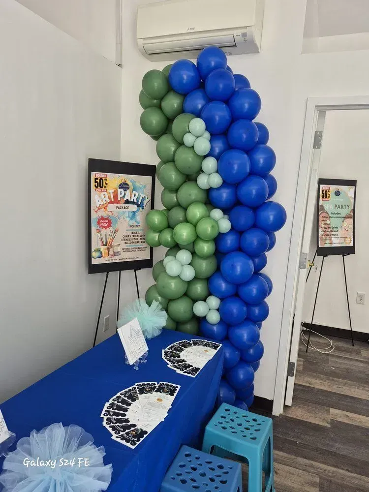 Blue and green balloon arch beside a blue table with flyers, in a small indoor event space