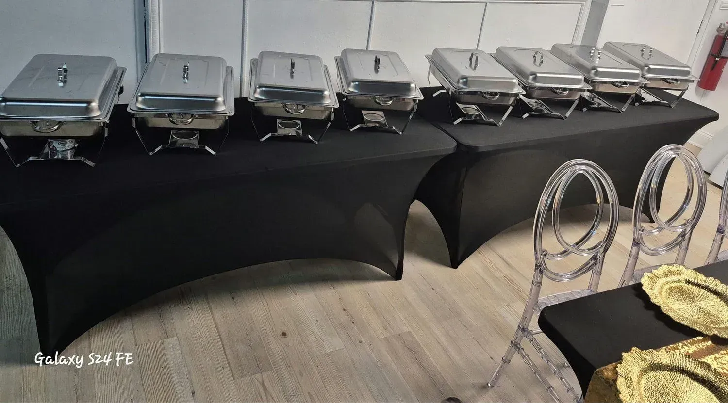 Rows of silver chafing dishes on black-covered tables in an indoor banquet setup