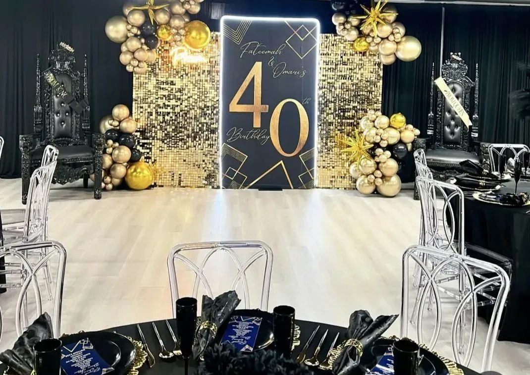 Black-and-gold 40th birthday party backdrop with balloons, lights, and decorated tables