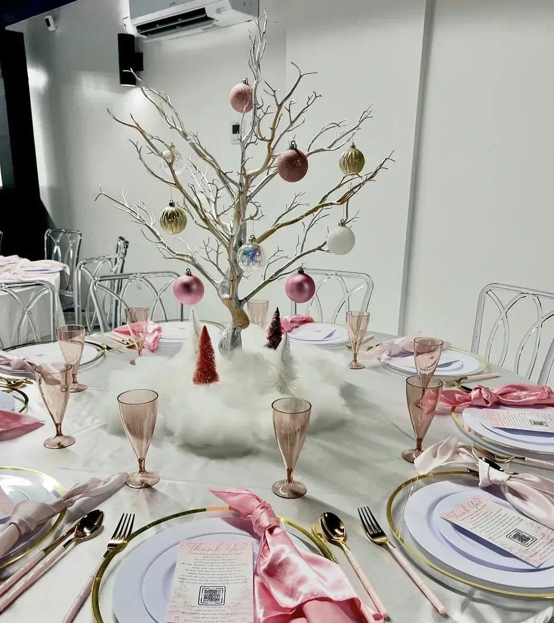 Elegant holiday table setting with pink accents, white plates, and a frosted branch centerpiece