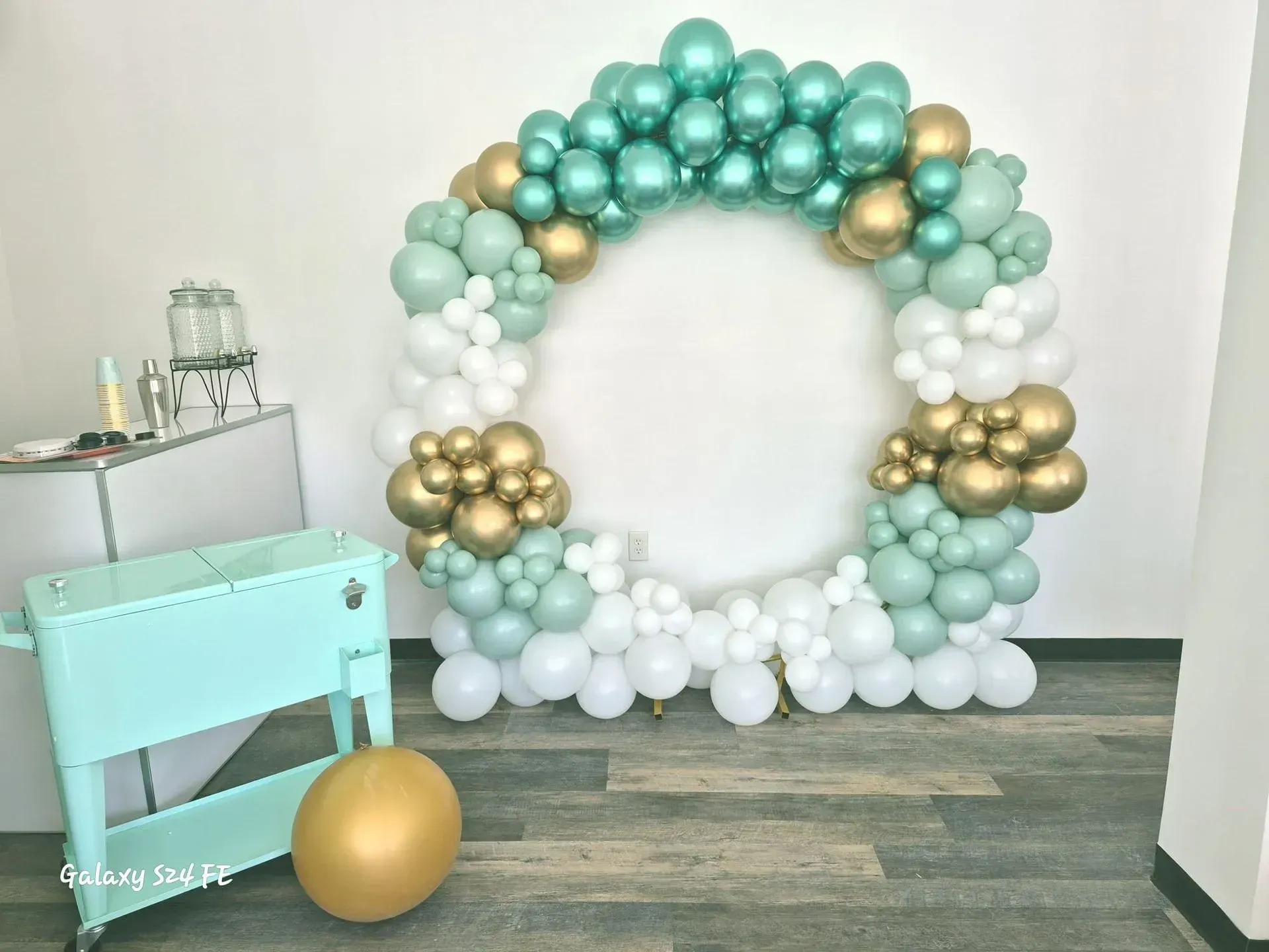 Mint and white balloon arch with gold accents in a decorated party setup, beside a small mint table.