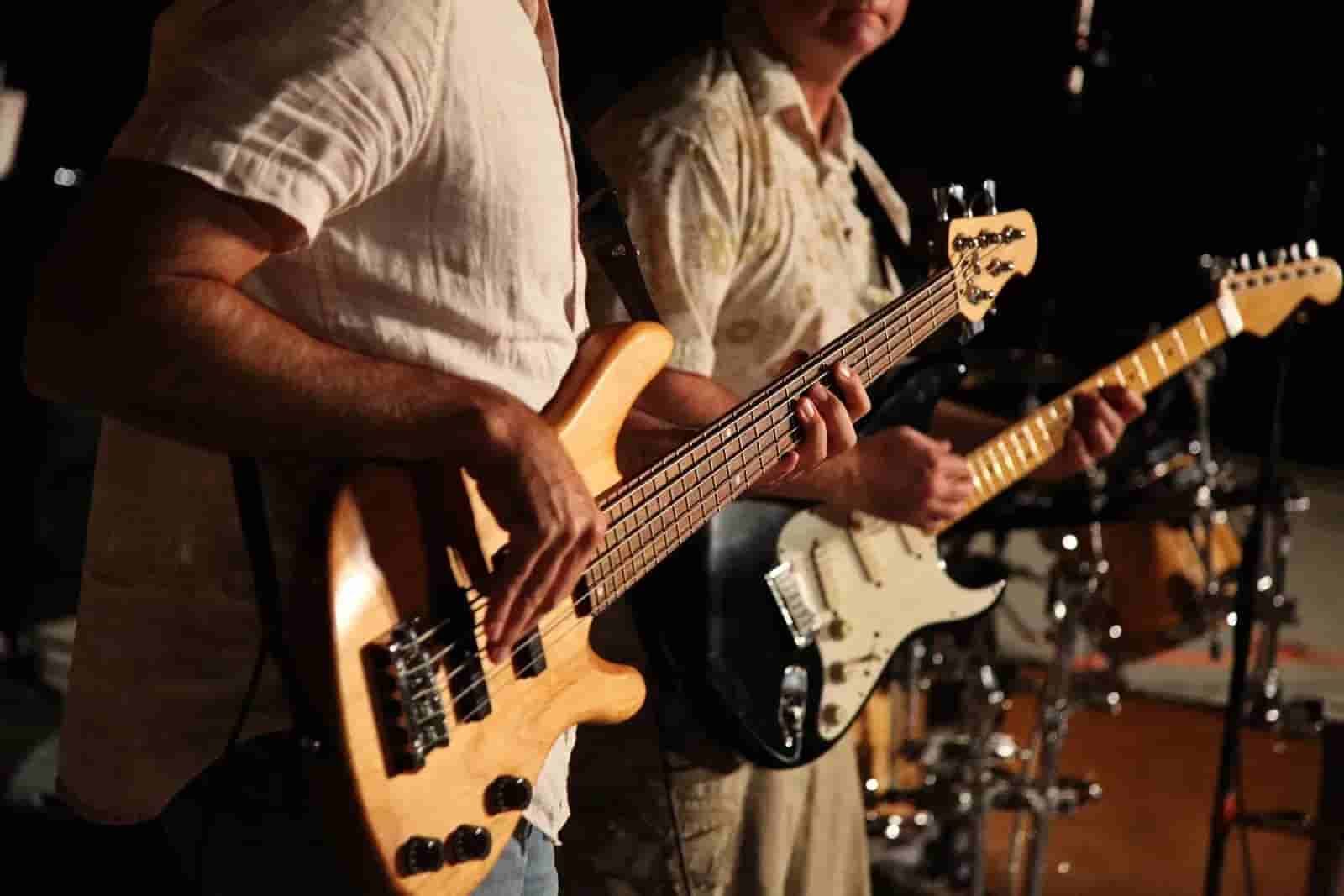 Two musicians playing electric bass and guitar on stage under warm stage lights