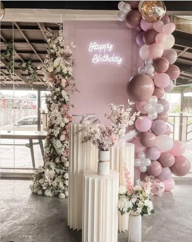 Pink and white baby shower backdrop with balloons, flowers, and a central display table