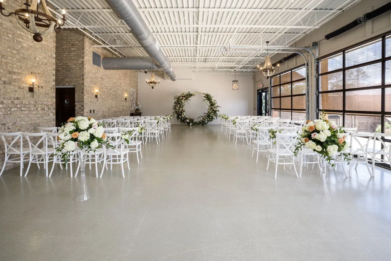 Elegant indoor wedding venue with white chairs, floral arrangements, and a circular greenery arch
