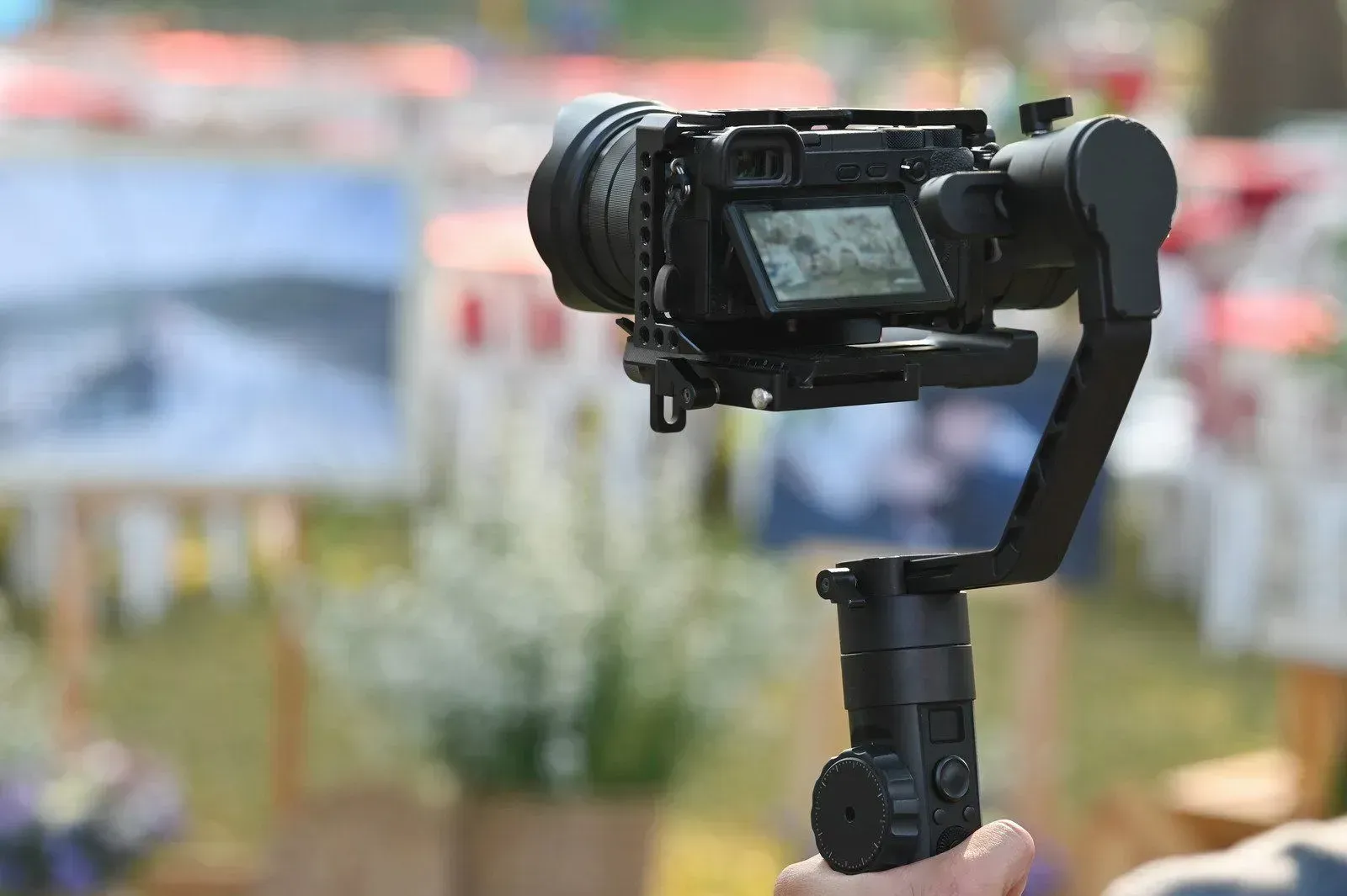 Handheld camera on a gimbal, filming outdoors with a blurred event scene in the background