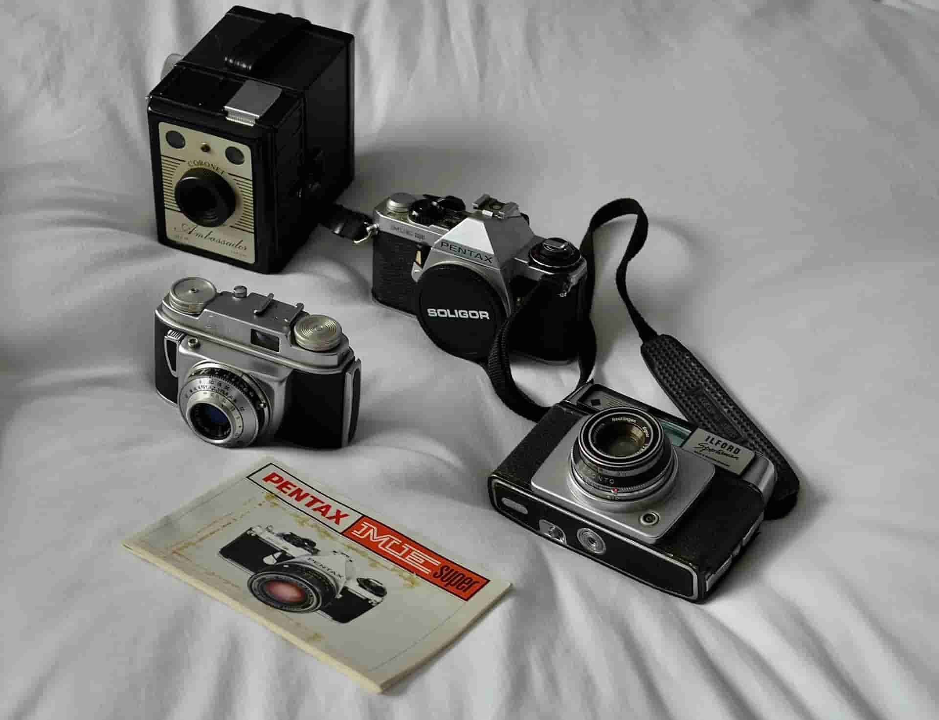 Four vintage cameras and a camera manual arranged on a white cloth background