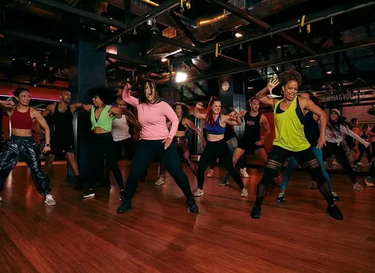 Group fitness class in a mirrored studio, people dancing in colorful workout clothes