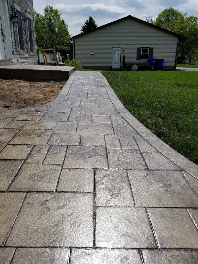Stamped concrete walkway leads to a beige building with green lawn on the right.