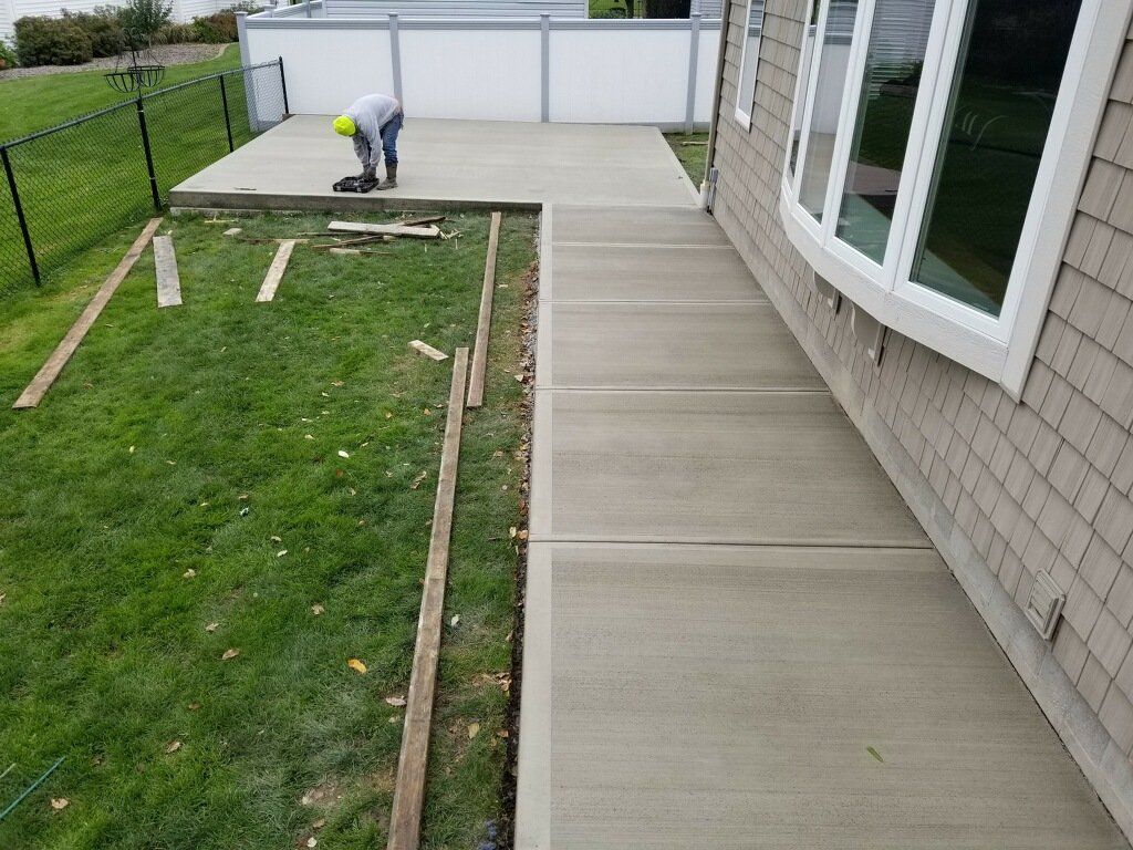 A person working on a concrete patio and walkway next to a house with a green lawn.