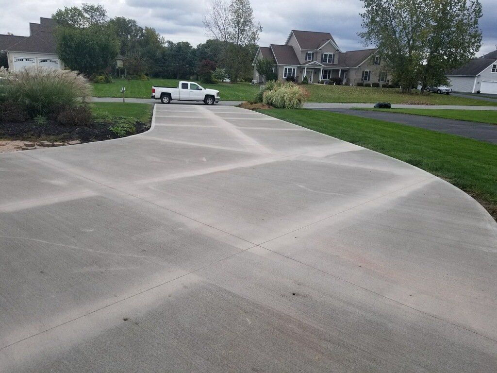 A concrete driveway with a crisscross pattern, a white truck, and a large house in the background.