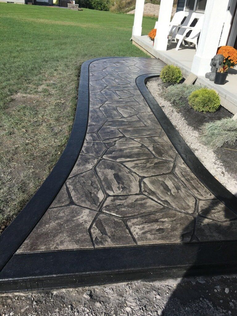 Stamped concrete walkway with a black border, leading to a porch with fall flowers.