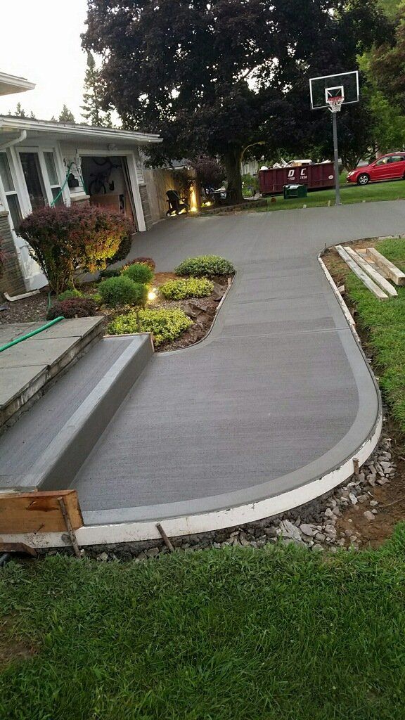 Newly poured concrete walkway and steps leading to a house with landscaping and a driveway.