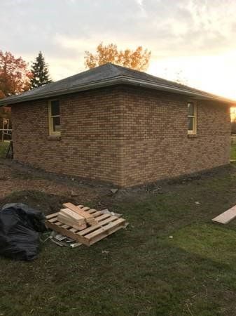Brick building with yellow window frames and a dark roof; construction site with a pallet of wood.
