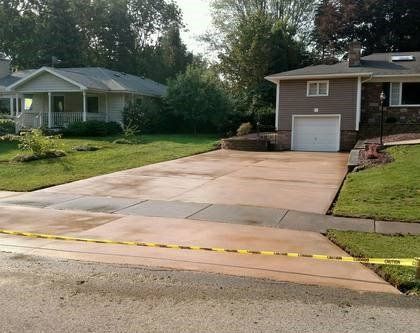 A house with a newly poured concrete driveway, yellow caution tape on the edge, and adjacent green lawn.