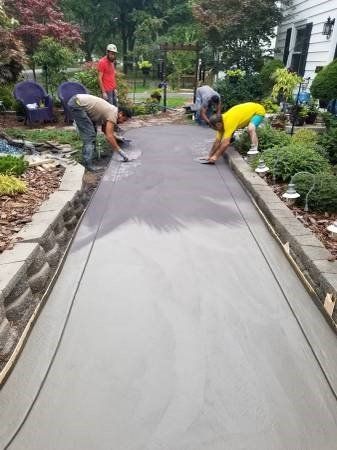Workers smoothing wet concrete for a pathway in a garden setting.