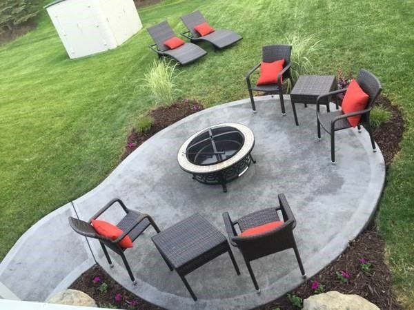 Outdoor patio with fire pit, seating, and lounge chairs on a grassy lawn.