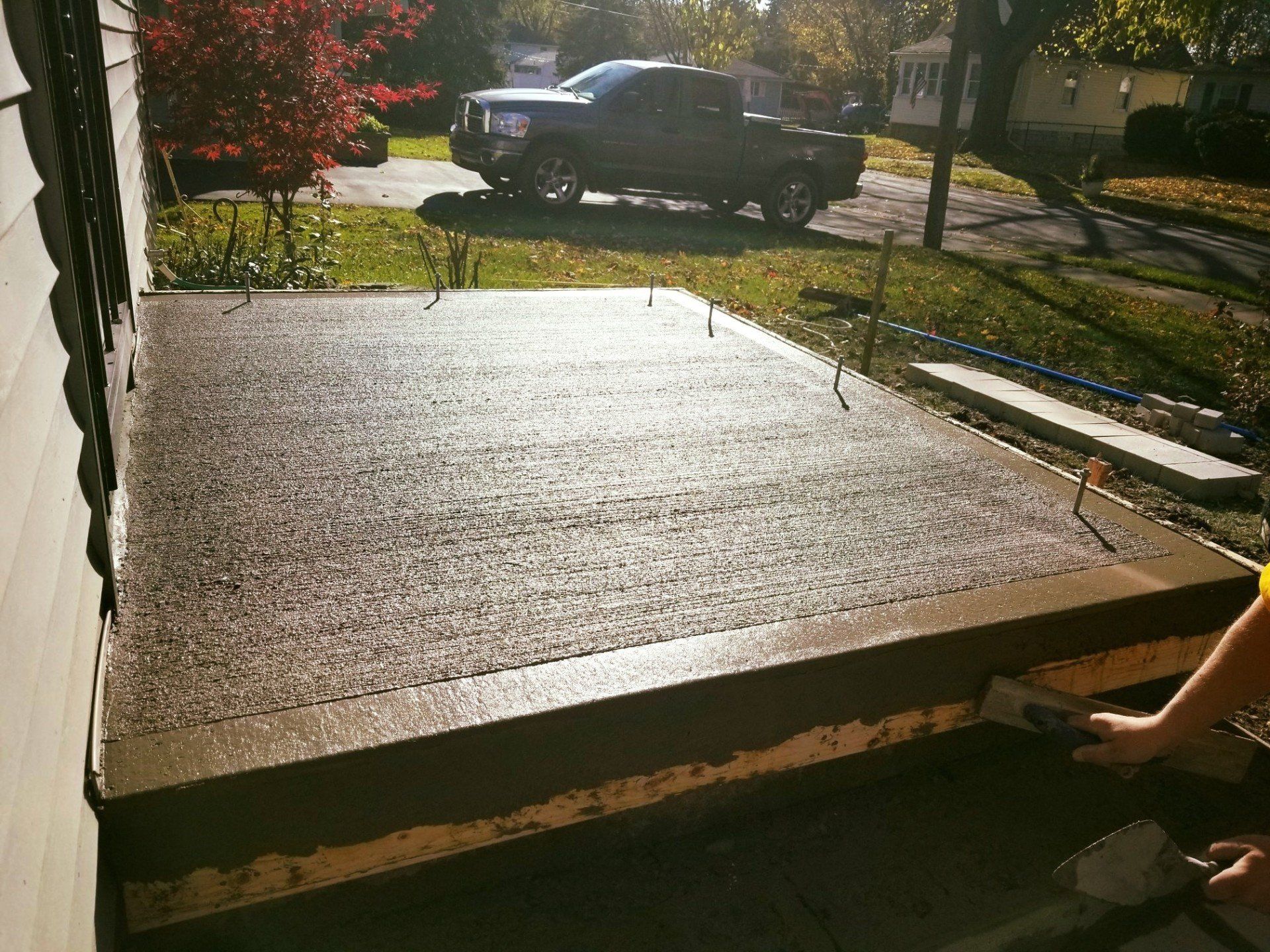 Freshly poured concrete porch with a person troweling it. A pickup truck is in the background.