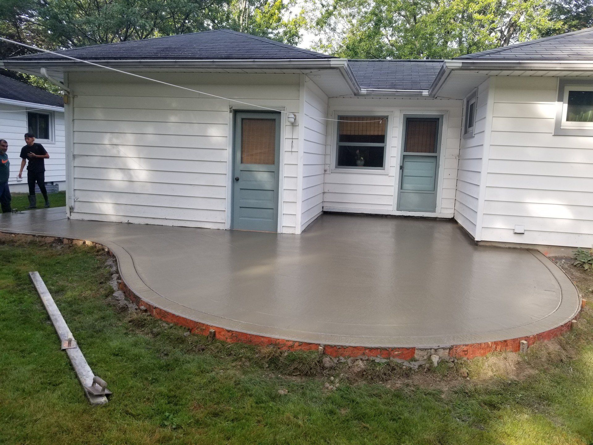 Freshly poured concrete patio with brick edging next to a white house.