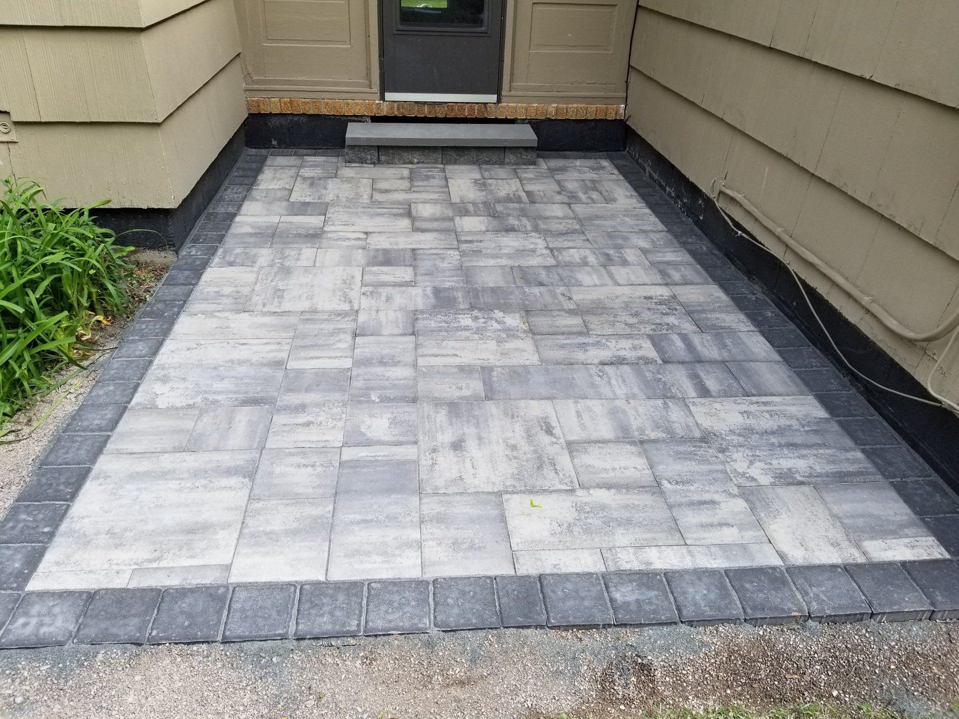 Stone patio with dark border in front of a house entrance.