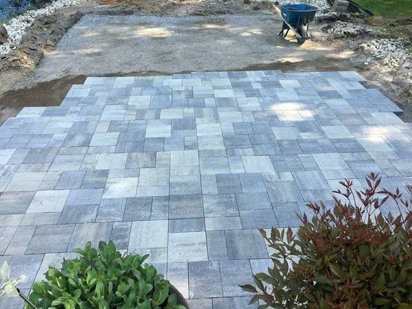 Patio being constructed with gray pavers, with dirt and wheelbarrow in the background.