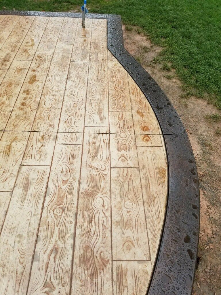 Stamped concrete patio with wood grain pattern, dark gray border, and curved edge.