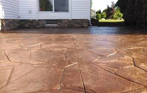 Brown stamped concrete patio with stone-like pattern in front of a white house.