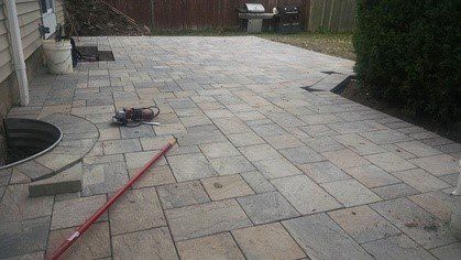 Paver patio with a circular inset, a red tool, and a grill in the background.