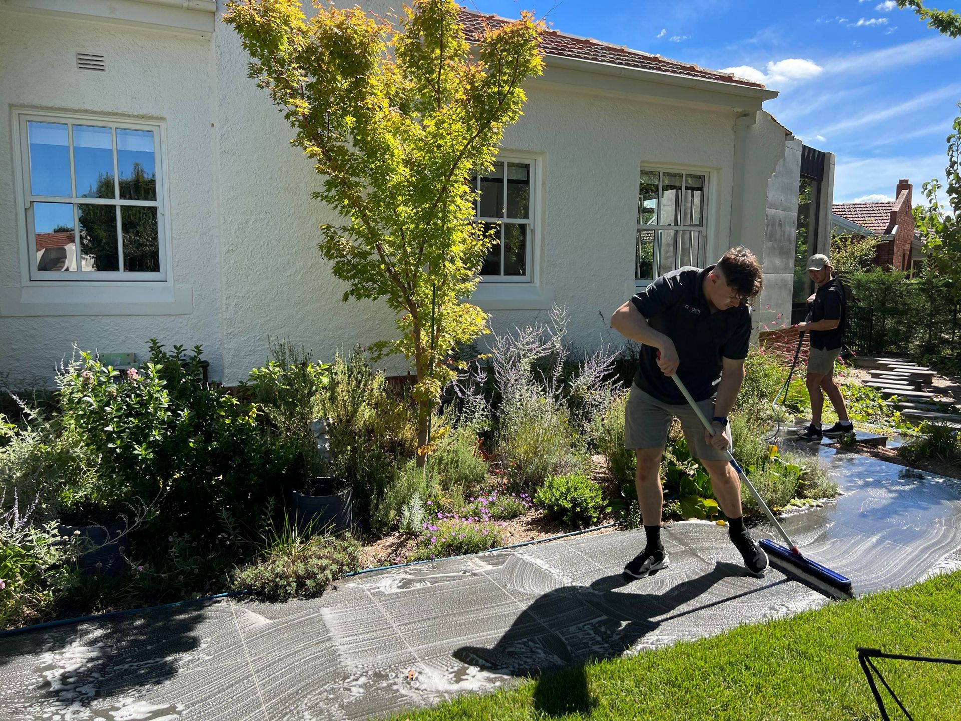A man is cleaning the sidewalk in front of a white house.