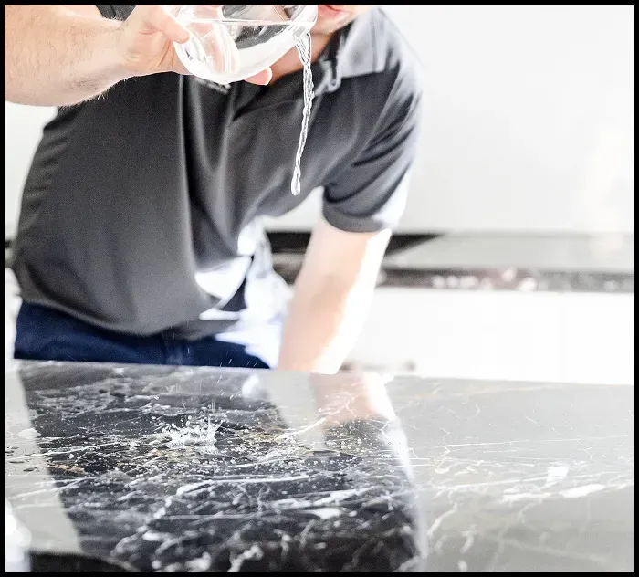 Man pouring water on marble to test sealant or illustrate cleaning importance