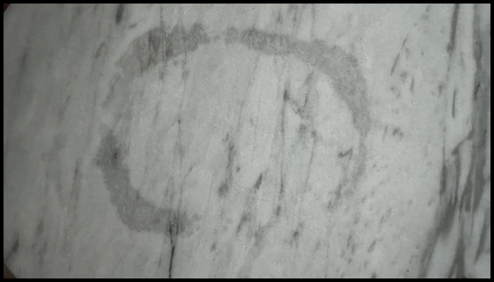 Dark ring-shaped oil stain on white marble surface