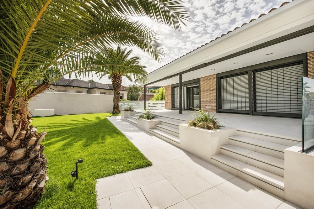A house with a lush green lawn and palm trees in front of it with marble steps.